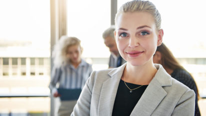 Portrait of a smiling young businesswoman standing in a bright modern office with a group of colleagues working in the background